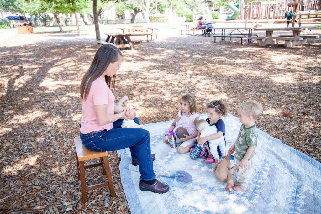 Tania teaching a childbirth education class to kids at Libbey Park. Kids are watching with dolls in their laps.