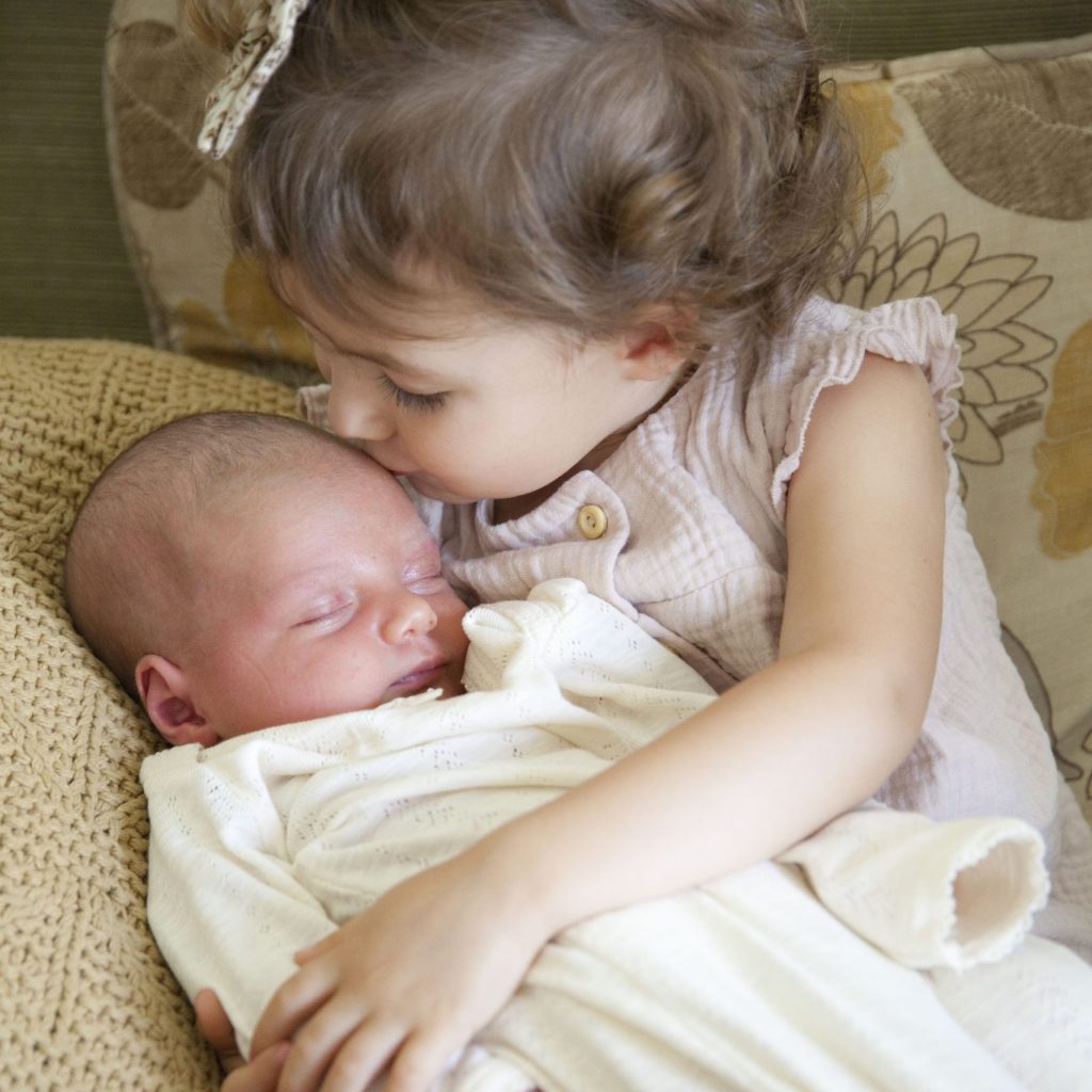 New big sister holding her new baby and kissing her on the head.