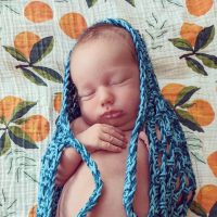 Newborn sleeping in a baby sling after being weighed at home. Baby is laying on a blanket printed with oranges.